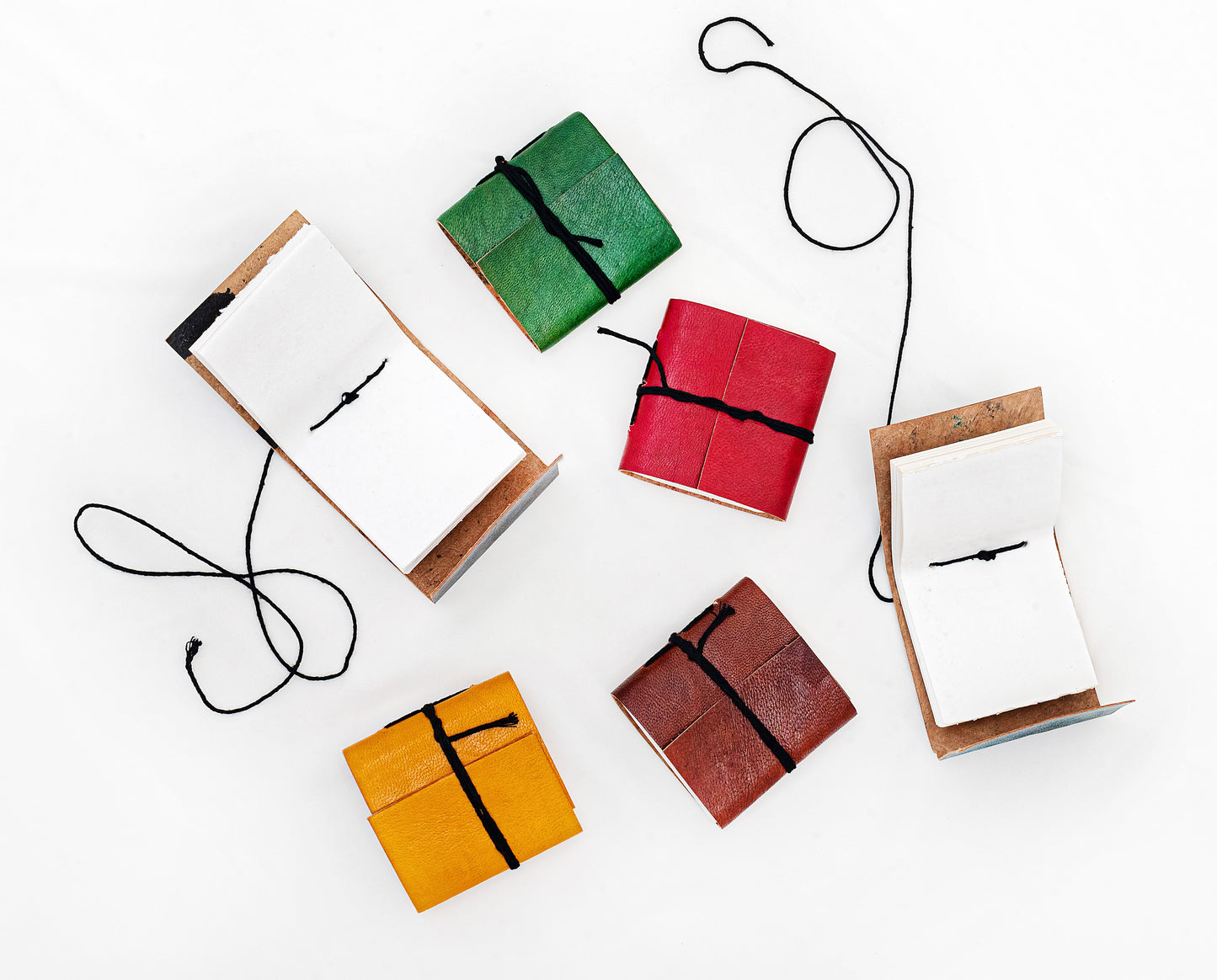 Mini carnets artisanaux en cuir coloré avec fermeture par cordon noir, couleurs aléatoires sur fond blanc