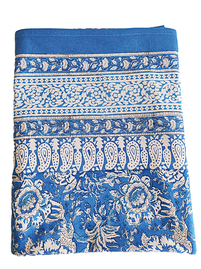 Nappe rectangulaire 6 places en coton Block Print indien bleu et écru, motifs floraux et cachemire, présentée pliée et dressée sur une table extérieure.
