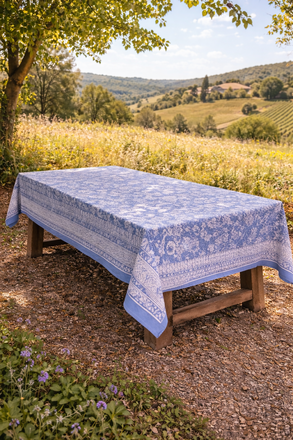 Nappe rectangulaire 6 places en coton Block Print indien bleu et écru, motifs floraux et cachemire, présentée pliée et dressée sur une table extérieure.