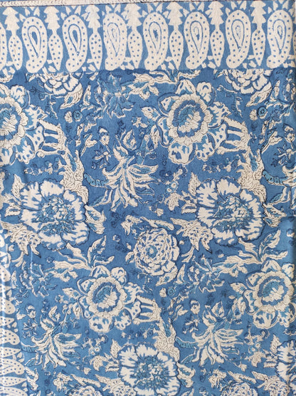 Nappe rectangulaire 6 places en coton Block Print indien bleu et écru, motifs floraux et cachemire, présentée pliée et dressée sur une table extérieure.
