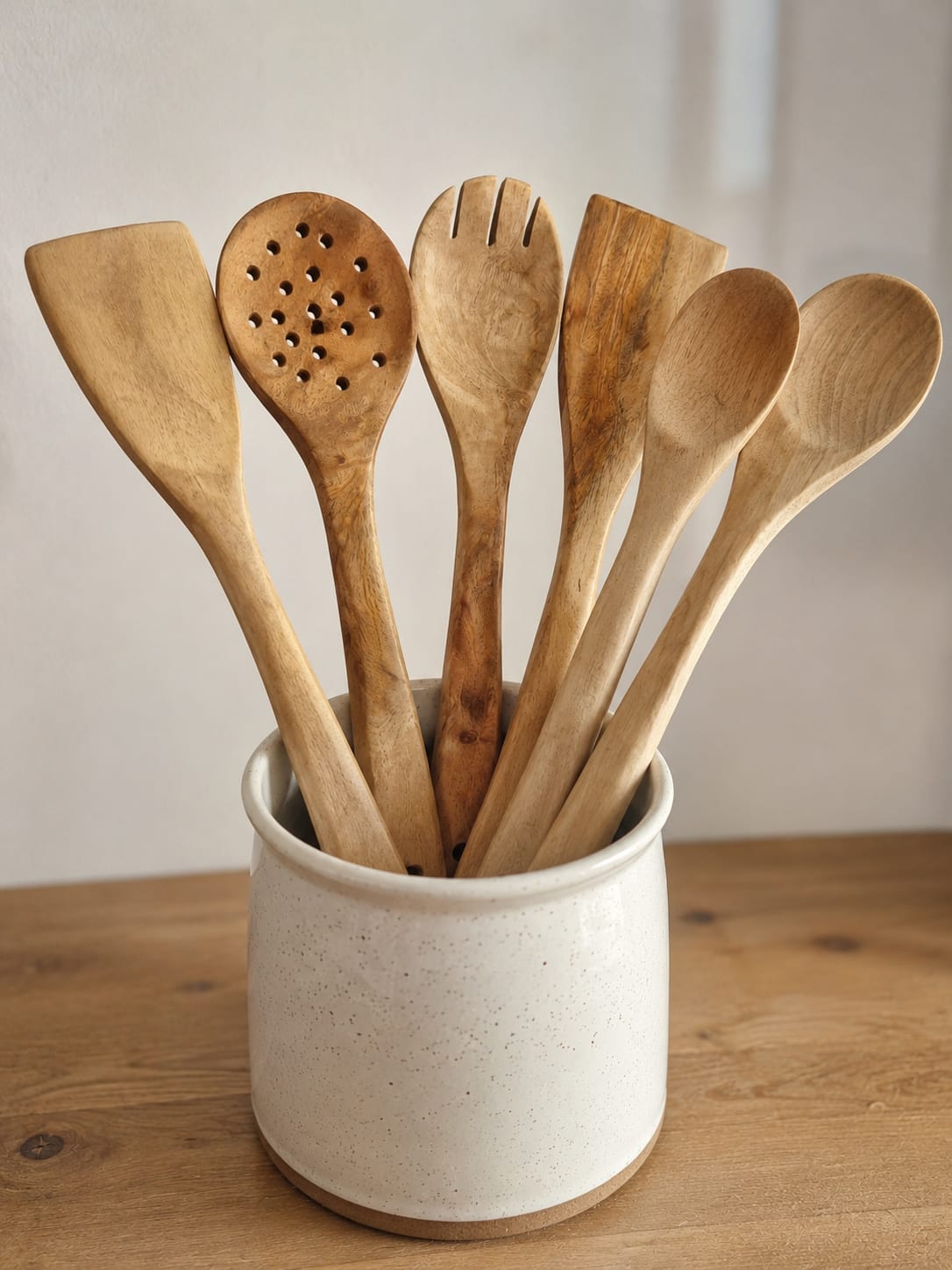 Set de 6 ustensiles de cuisine artisanaux en bois de Neem naturel avec cuillères, spatules, fourchette et écumoire sur fond blanc.