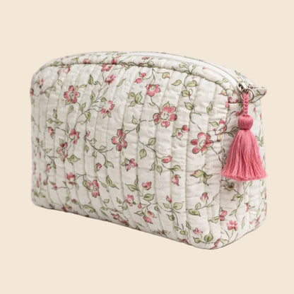 Trousse de toilette matelassée blanche From India Boutique, en coton imprimé floral artisanal rose, vert et taupe, avec étiquette cousue et pompon rose, présentée sur fond beige.