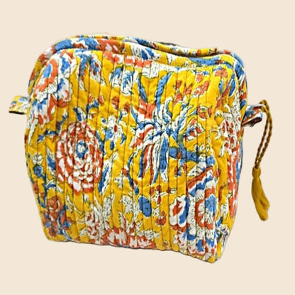 Trousse de toilette XL matelassée jaune From India Boutique, en coton imprimé floral artisanal, avec fermeture zippée et pompon jaune, présentée sur fond beige.
