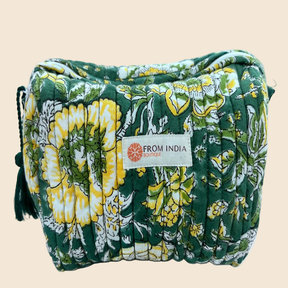 Trousse de toilette matelassée verte From India Boutique, en coton imprimé floral jaune et blanc, avec étiquette cousue et pompon assorti, présentée sur fond beige.